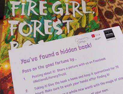 A photograph of a book with a postcard on top. Postcard says 'You've found a hidden book!'. To promote event at Hastings Museum.
