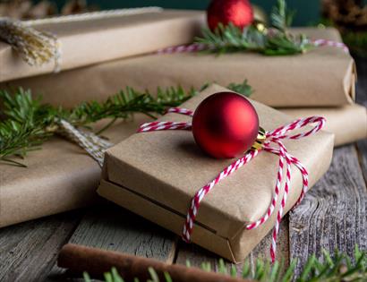 photograph of parcel-wrapped gifts with red bauble and sprigs of christmas tree.