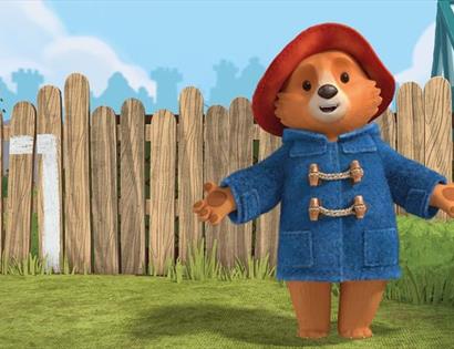 poster of cartoon bear in front of a garden fence wearing a blue duffle coat and a red hat.