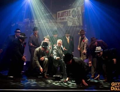 A group of men dancing on stage wearing suits and trilby hats.
