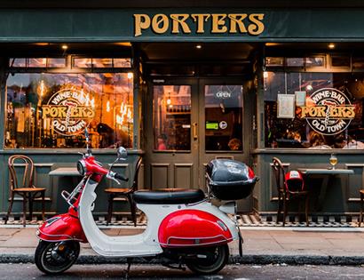Exterior of Porters Wine Bar with gold handpainted sign and a moped scooter in front.