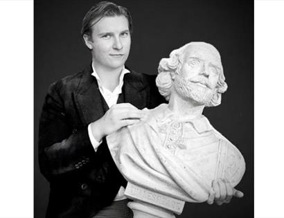 A black and white photograph of a white man holding a bust of Shakespeare.