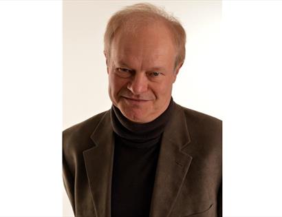 a photograph of a white man wearing black roll neck sweater and blazer.