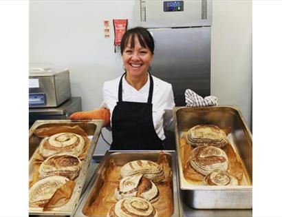 lady in apron holding trays of baked sourdough loaves