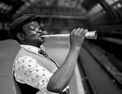photograph by bob mazzer man on train platform blowing a horn instrument