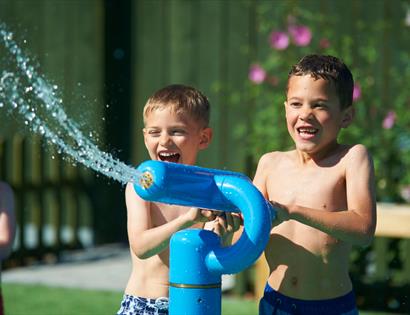 Three young boys dressed in swimming trunks, playing with a fun water sprinkler. 