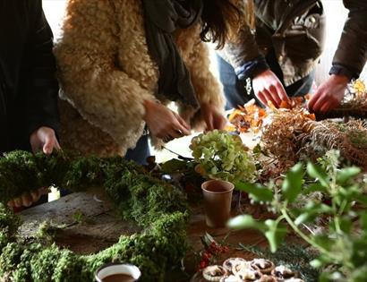 close of workbench with hands busy preparing christmas wreaths with moss and foliage.