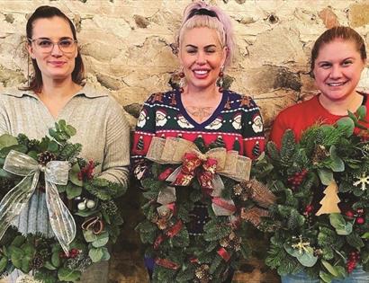 Three women hold up Christmas wreaths.