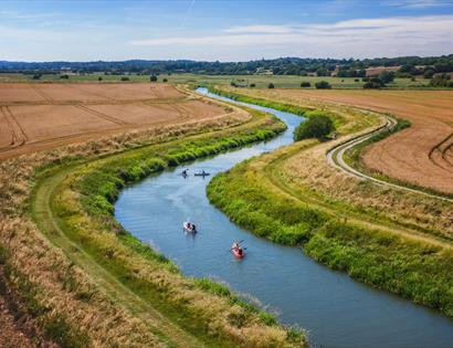 Aerial view Bodiam Boating Station, with blue waterways
winding through green marshland under a clear sky with people doing water sports.