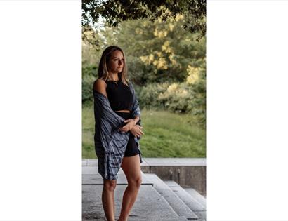 Image shows a person stanading outside looking into the distance. They are dressed casually for yoga and look like they are reflecting.