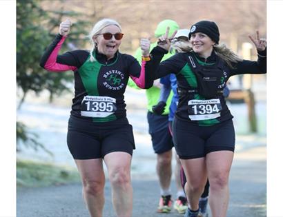 Action shot of two women competing in an outdoor race, focused and energetic, with crowd barriers and city street in the background.