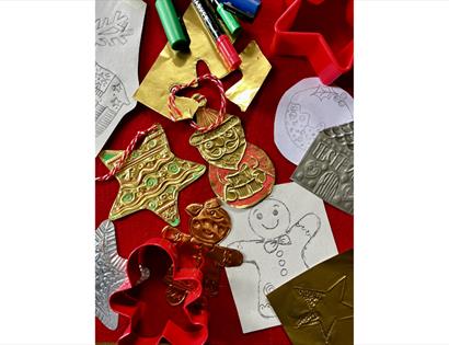 Overhead view of DIY holiday ornament making. Mixed materials include shiny gold and silver foil pieces with stamped patterns, finished ornaments (tre