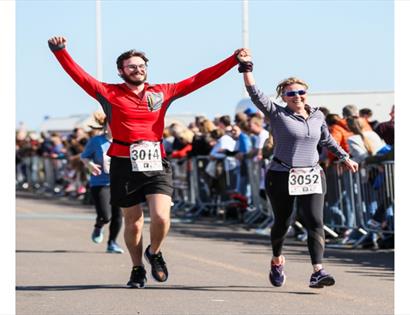 Focused runners mid-stride during an outdoor street race, urban backdrop with barriers and onlookers.