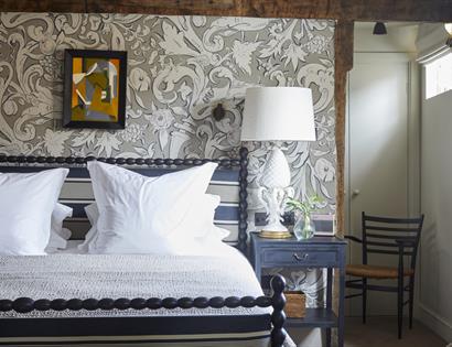 interior view of bedroom shows decorative wallpaper, wooden chair, and deluxe double bed with white sheets