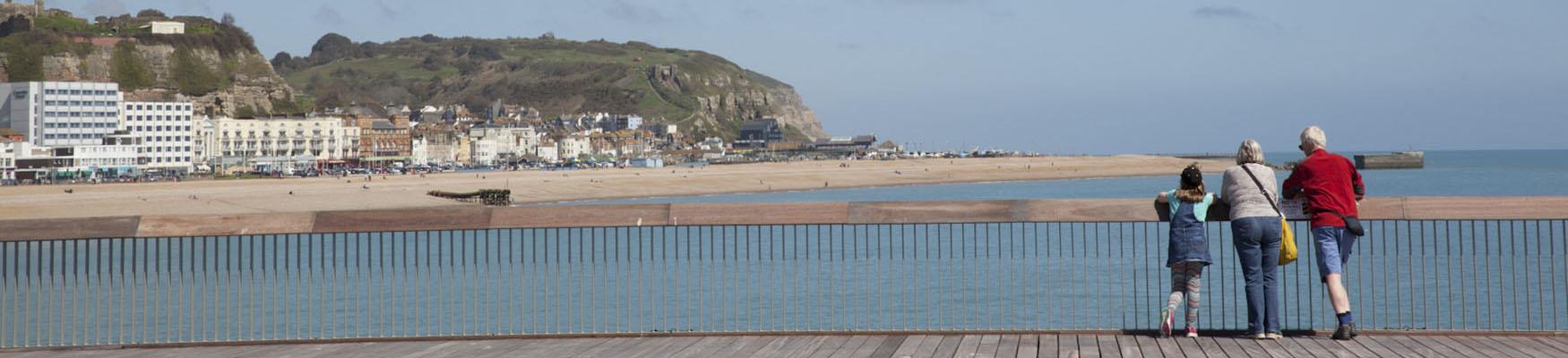 3 people standing on the pier looking at view of Hastings seaside and East hill