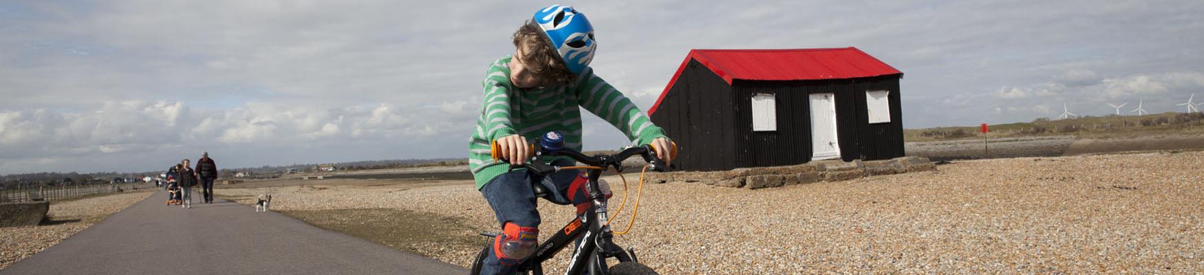 A young child riding a bike along a path in Rye, with a
red-roofed black shed and wind turbines in the distance.