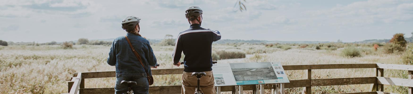 Cyclists pause at a viewing platform overlooking Rye Harbour Nature Reserve and its expansive wetlands.