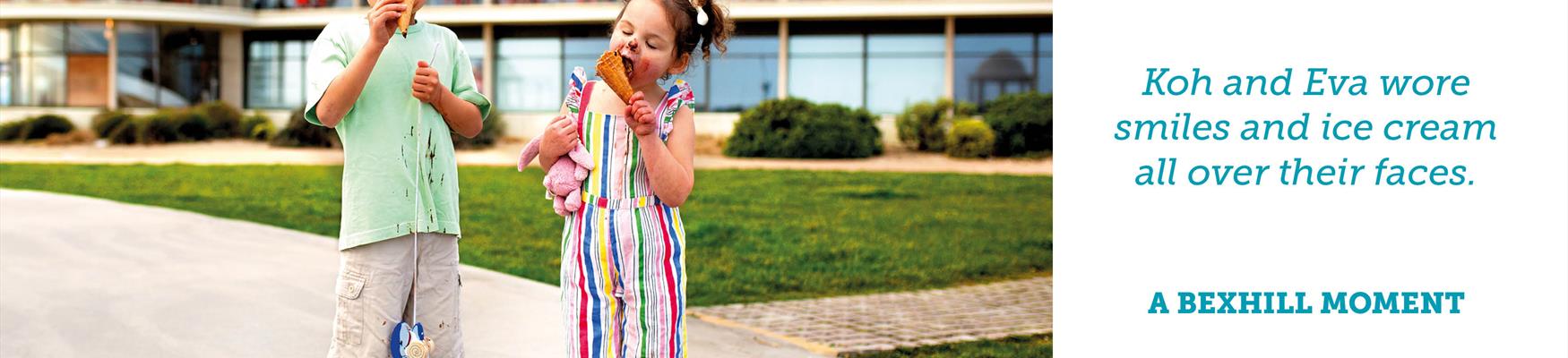 Two children standing outside the De La Warr Pavilion with ice cream over their faces.