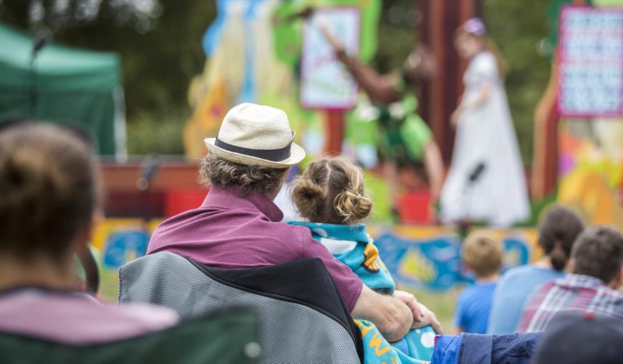 focus on backs of outdoor audience with performance blurred in the background