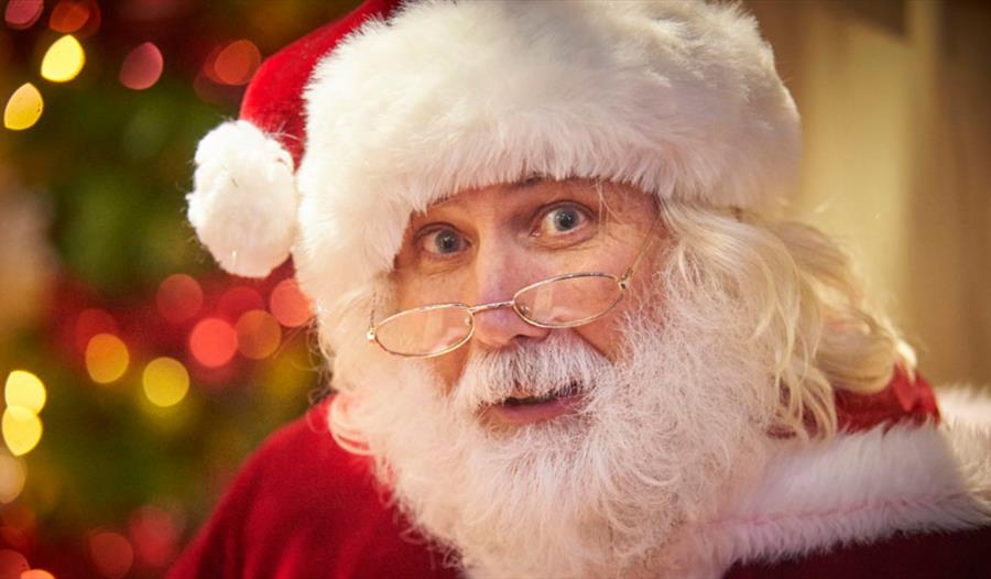 photograph of father christmas. A close up of a man witha white beard and moustache with red outfit and white-fur lined hat, spectacles reading on nos