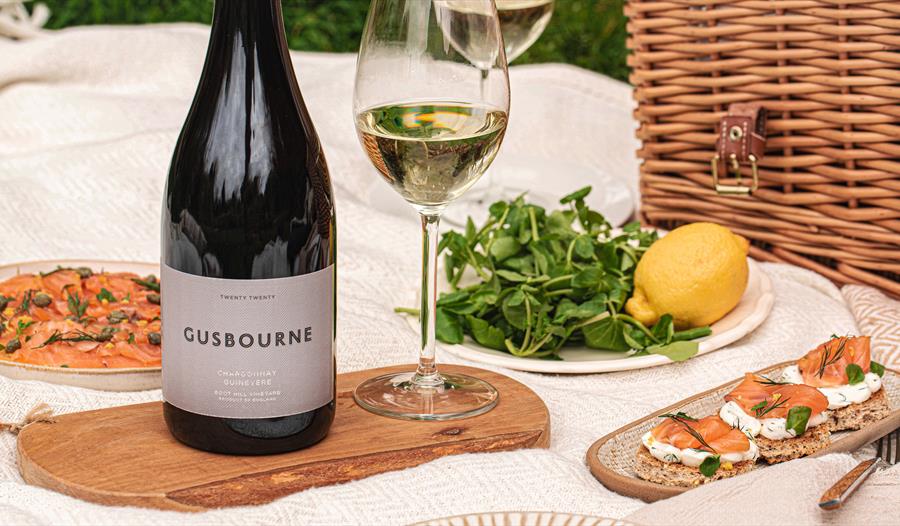 close up shot of picnic blanket laid with gusbourne wine, salmon canapes and rocket and lemon, hamper in background