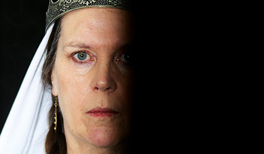 close up portrait of a white woman staring coldly at the camera, one half of face in complete shadow, a crown slightly visible