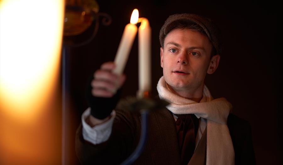 a young man wearing a cap and scarf lighting a candle.