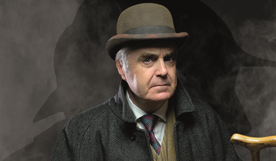 a portrait of a white man in a bowler hat, tie and coat. Background is dark and smokey.