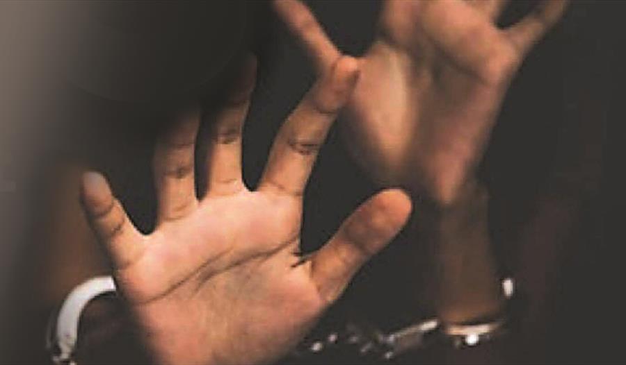 a photograph of a black person's hands reaching towards the camera with a blurred background. Handcuffs just visible.