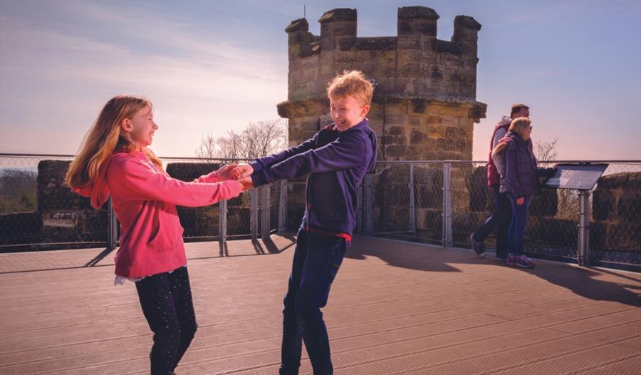 photograph of two children holding both hands on viewing platform with turret.