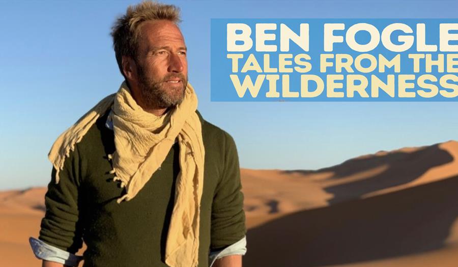 a poster for ben fogle tour at white rock. White man stands in the desert wearing a green top and biege scarf. top right text says ben fogle tales fro