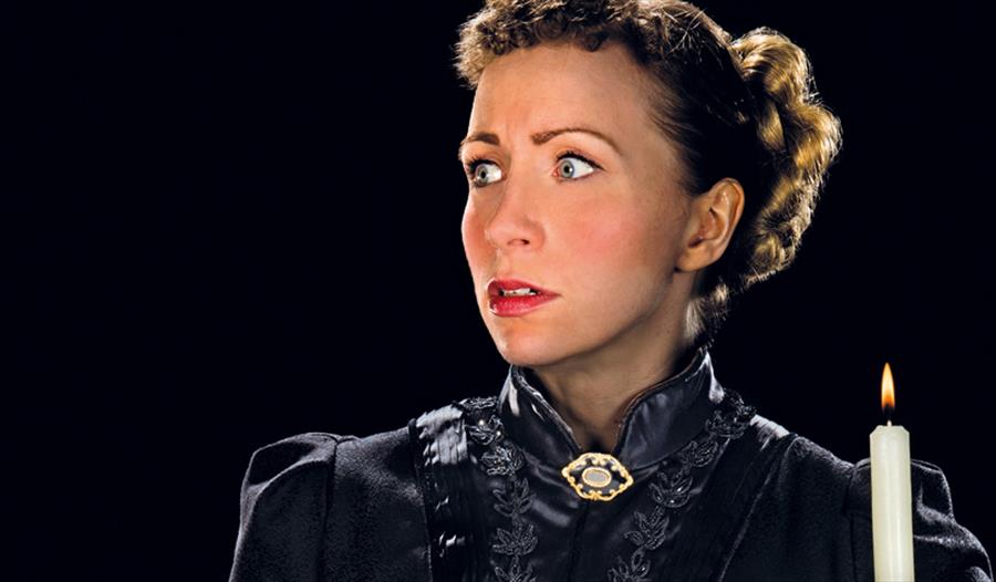 A photograph of a woman with a shocked expression holding a torch in the darkness