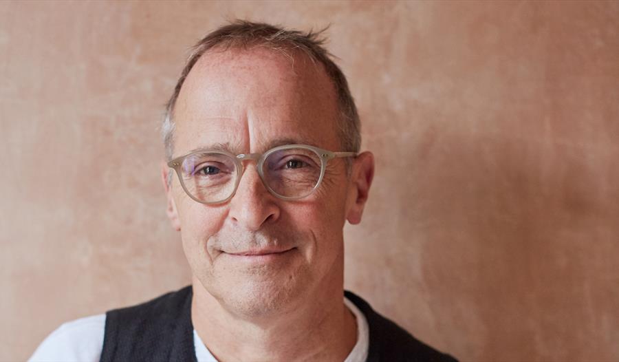 A close up of a white man smiling, wearing plastic rimmed glasses.
