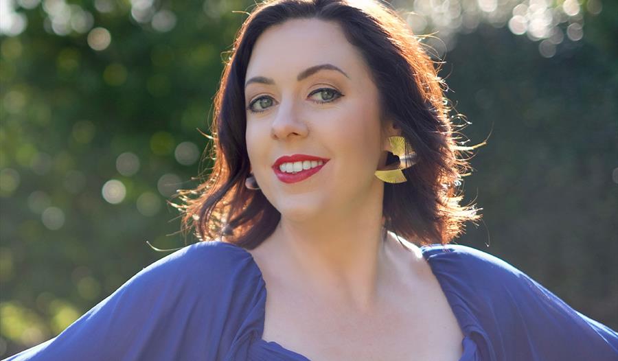 Headshot photograph of a woman smiling with red lipstick, she wears a blue dress