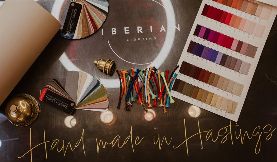 Fabric swatches, colour samples, and lighting materials arranged on a table with the text 'Hand made in Hastings'.