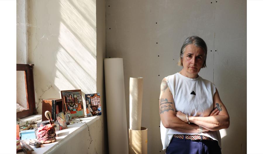 Artist standing in a sunlit studio beside artworks featured in the Finders Keepers exhibition.