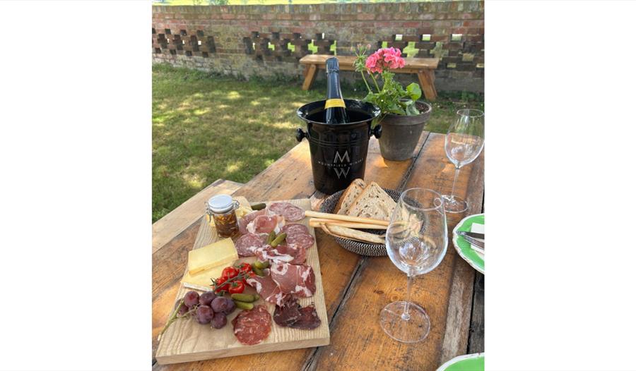 Outdoor table set with charcuterie, bread and glasses, alongside a chilled bottle of Mountfield wine in an ice bucket