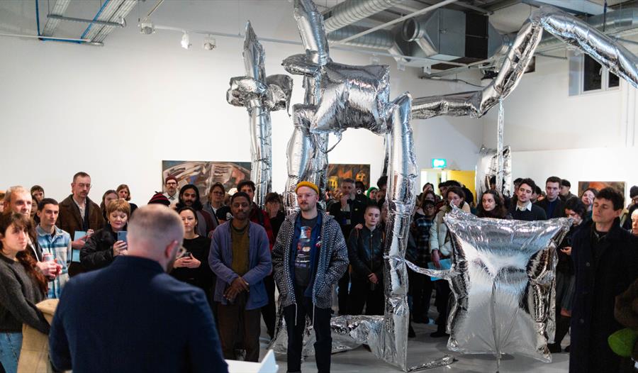 Crowd gathered around silver inflatable sculpture at Flatland Projects gallery opening in Bexhill.
