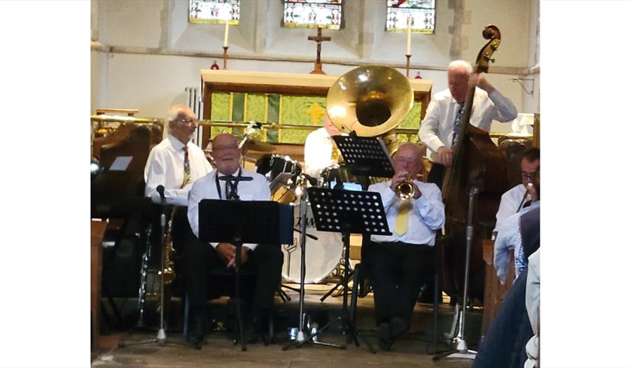 Live performance by John Arthy’s Rhythmic Hot Five in a church setting in Pevensey, with musicians playing brass and double bass.