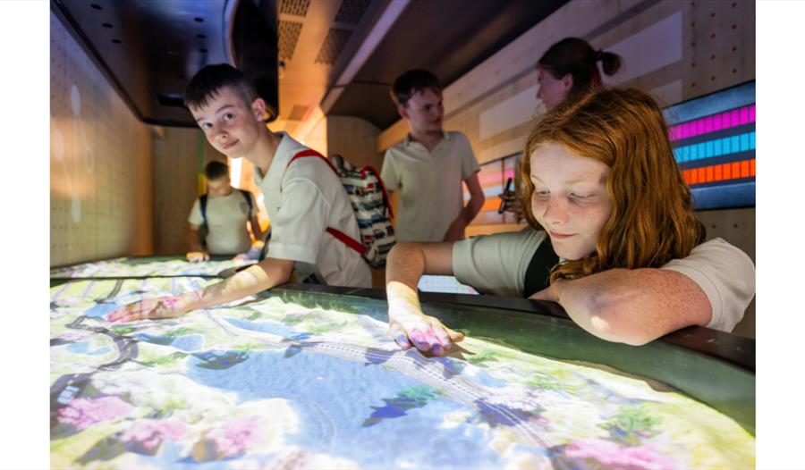 People exploring a free exhibition train and interacting with a large illuminated display.