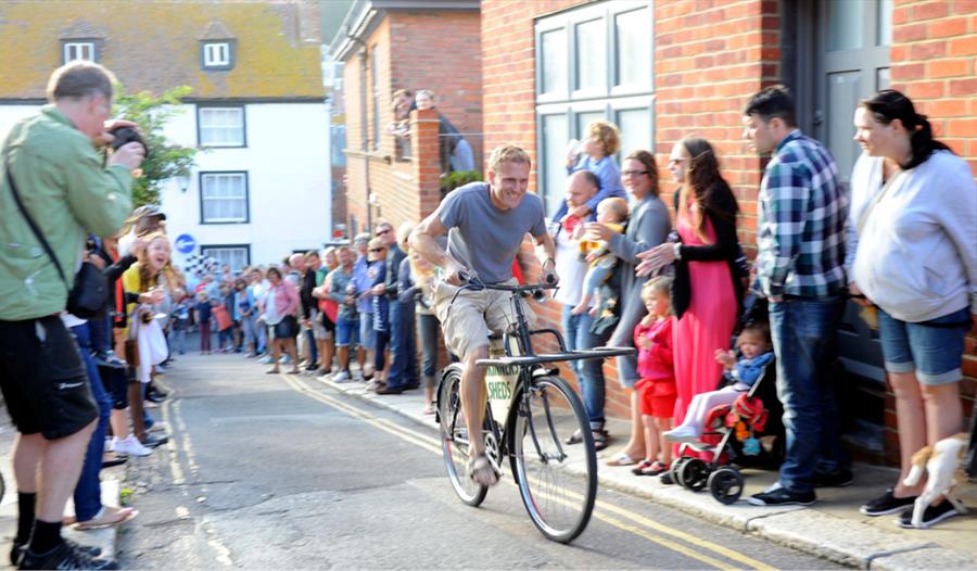 Hastings Old Town Carnival Week bicycle race draws crowds along a narrow street lined with spectators.