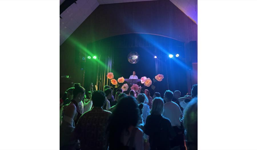 Crowd dancing beneath colourful lights and a disco ball at Rye Discotheque in a lively music venue.