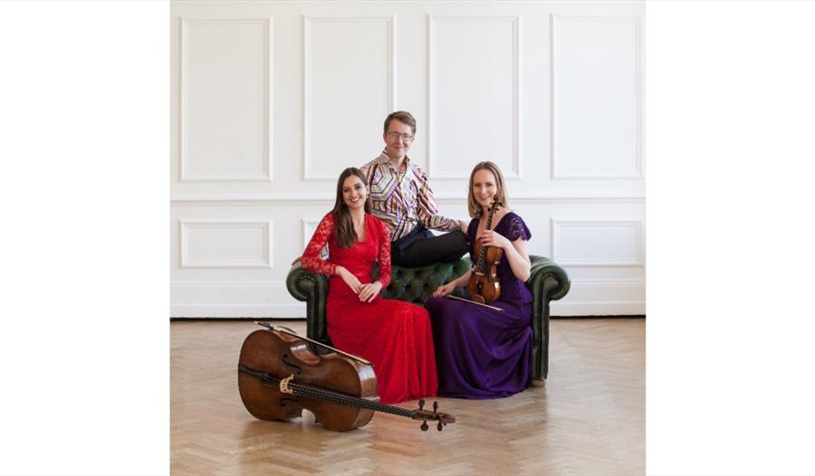 Rautio Piano Trio seated with cello and violin in a bright recital room, promoting a Winchelsea Arts concert.