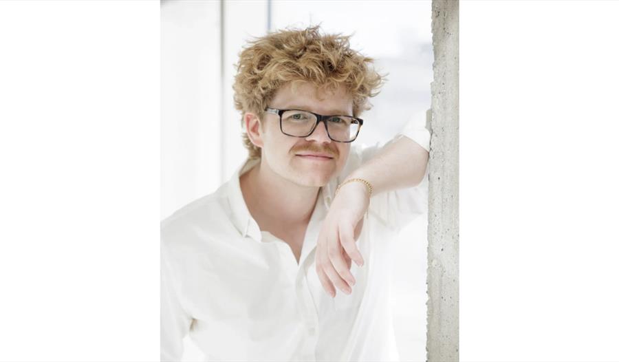 Promotional portrait for pianist Carter Johnson wearing glasses and a white shirt in a bright studio setting