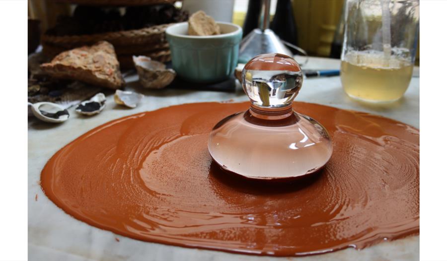 Glass muller grinding red pigment paste on a slab during a pigment‑making workshop.