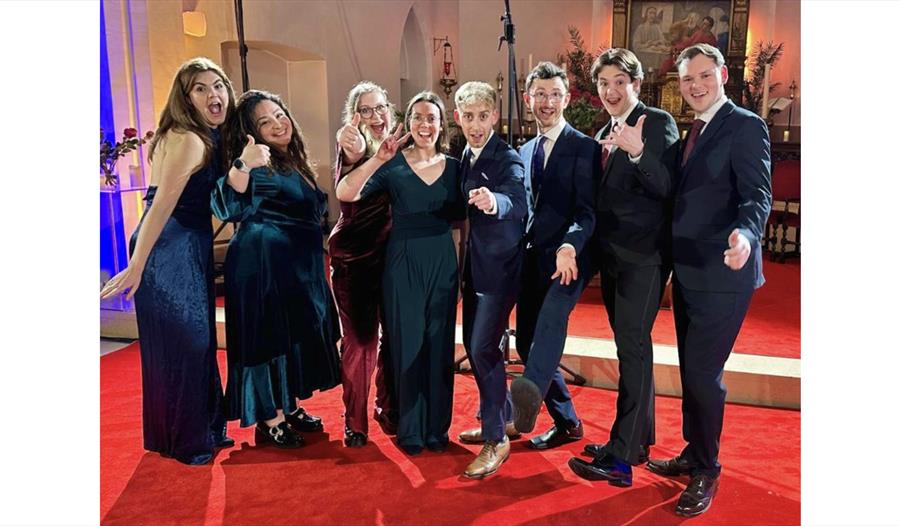 VOCES8 Scholars Ensemble members posing together in formal concert attire inside a church performance venue