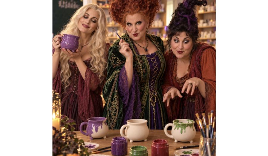 Three Hocus Pocus-inspired characters painting pottery mugs at a themed food and pottery painting event.