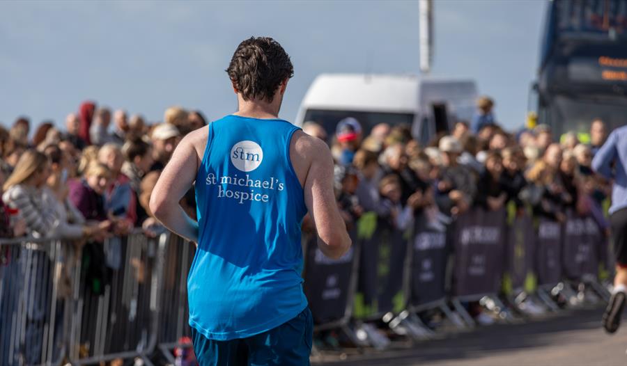 Promotional image for St Michael’s Hospice Run, showing a runner passing spectators along a race route.
