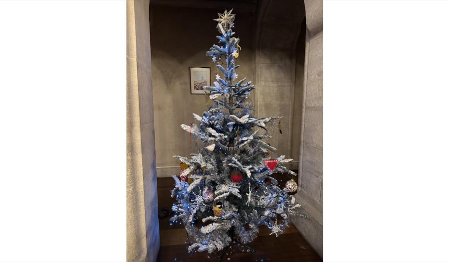 Decorated Christmas tree with silver tinsel, ornaments, and lights in a stone archway.