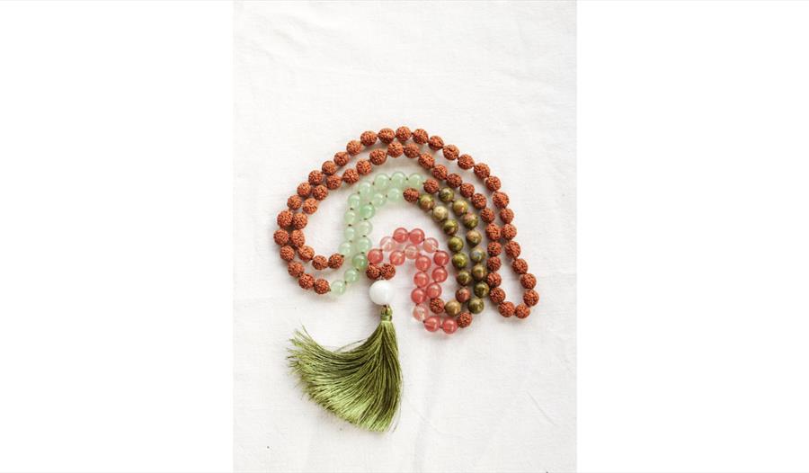 Beaded mala necklace with wooden and stone beads arranged in a spiral on white fabric, finished with a green tassel.